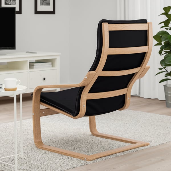 A black cushioned reclining chair with wooden frame, situated on a rug in a living space, featuring a footrest and high back support.
