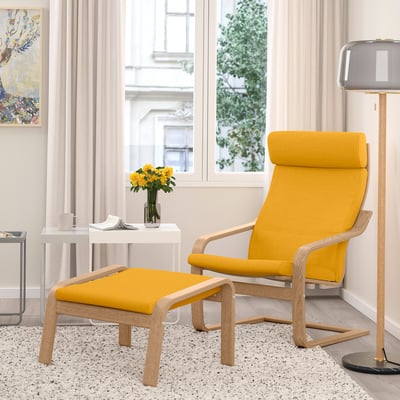 Yellow mustard POÄNG chair with footstool, side table, lamp, and flowers by a window.