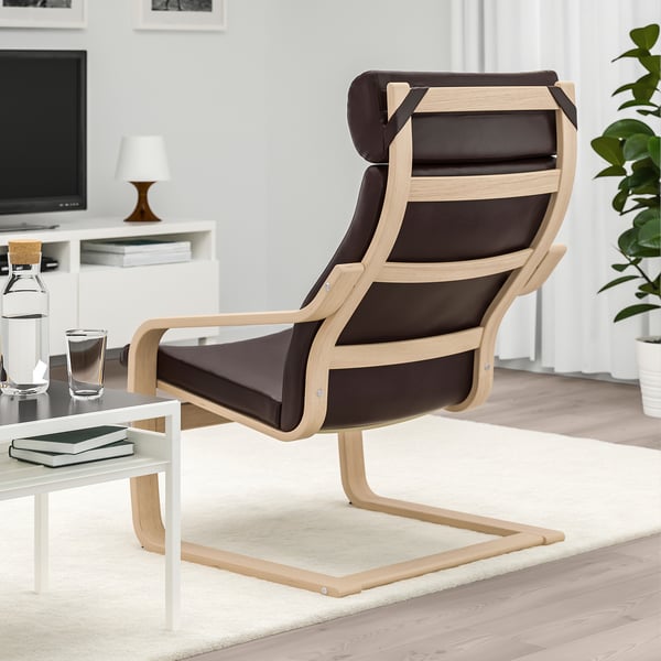 Modern armchair with wooden frame and dark cushions sits on a white rug. Beside it, a coffee table holds a glass, book, and water bottle.