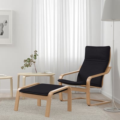 Black POÄNG chair and footstool near window with curtains, adding comfort and style.