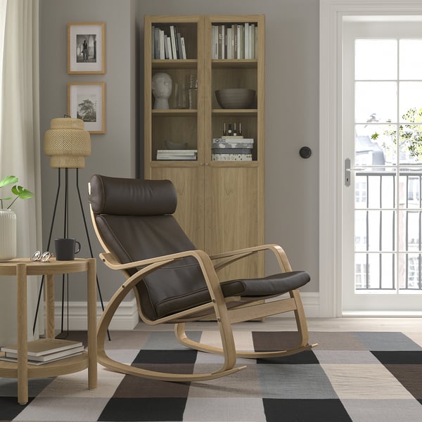 Modern living room with checkered rug, bookshelf, POÄNG chair, natural light, photos, lamp, plant.