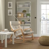Rocking chair POÄNG with cushions on rug, next to table and book shelf.