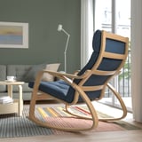 A minimalist room with a light wooden rocking chair, blue cushion, gray sofa, and side table near a large window.