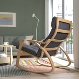 Modern living room with light wood rocking chair, grey cushions, striped rug, coffee table, sofa, and floor lamp by large window.