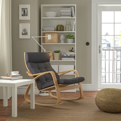 Modern living room with POÄNG chair. Dark grey cushioned chair, wooden frame, near white bookshelf. Cozy and inviting space.