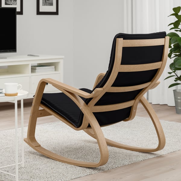 Modern rocking chair in a living room with wooden frame and black cushions. The chair is designed for comfort and relaxation.
