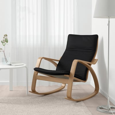 A cozy POÄNG armchair with a black cushion in a bright room. It a comfortable back support and a wooden frame, perfect for relaxing.