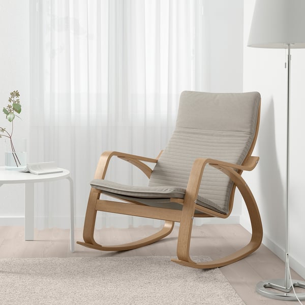 Modern wooden rocking chair with cushions in bright living space, next to table and floor lamp.