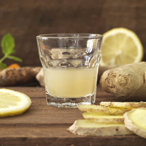 Glass filled with yellow drink, surrounded by ginger, lemon slices, highlighting its classic design suitable for various occasions and healthy drinks.