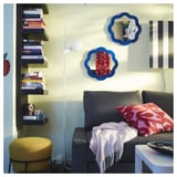 Cozy living room with grey sofa, red pillows, yellow stool, bookshelf, blue mirrors, lamp, and side table.