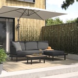 Modern black outdoor patio set with cushioned sofa, chaise, and wooden coffee table under large beige umbrella on a wooden deck.