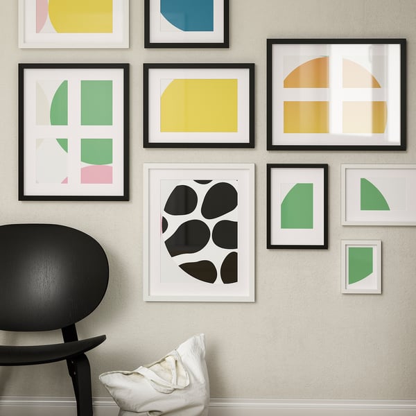 Modern art prints gallery wall, black & white frames, chair & pillow.