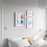Three RÖDALM frames above bed: left with shapes, others single blobs. White frames, largest left. Bed has grid pillows and yellow bolster.