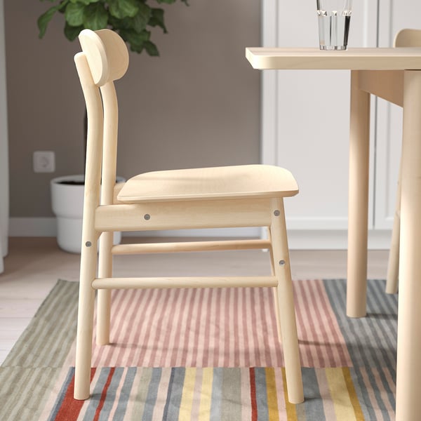 Light wooden chair with smooth curves; fits classic and modern spaces; placed on striped rug beside a table.