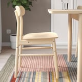Light wooden chair with smooth curves; fits classic and modern spaces; placed on striped rug beside a table.