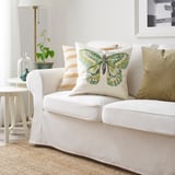Square ROTFJÄRIL pillow with butterfly design on a white couch, mix of colors, ramie & cotton, stands out.