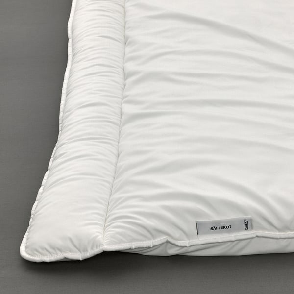 Close-up of a white quilt, neatly folded. Tag on edge reads SÄFFEROT.