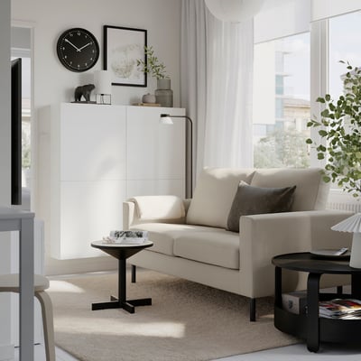 Modern living room: cream sofa, black tables, rug, clock, decor, white cabinet, window curtains.