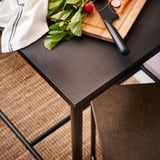 Black metal and wood kitchen table with vegetables, knife, and cloth.