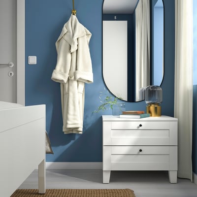 Modern bedroom with blue walls; white SANNIDAL bedside table, hanging robe, large mirror, and decorative pieces.