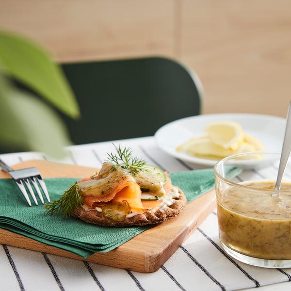Dish with green sauce, salad, and slice of bread. Served on a wooden board with fork and knife.