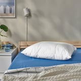 Modern bedroom, large white pillow on blue sheets, wooden headboard, minimalist decor.