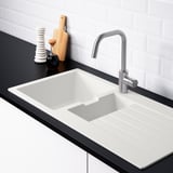 Modern kitchen sink with reversible drainboard, sloping water flow, two tap holes, white, black countertop, silver faucet, wooden cutting board.