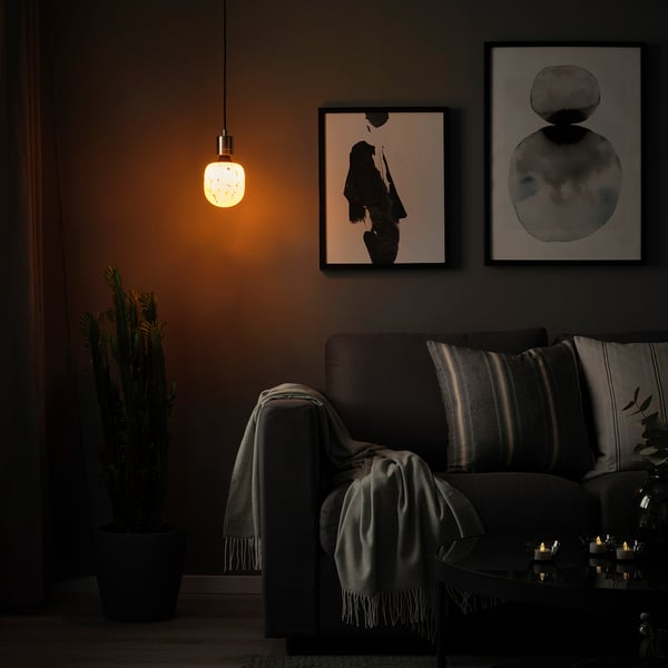 Cozy living room with SKAFTET lamp, couch, art, candles, and cactus.