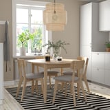 Modern dining set with light wood table, striped rug, hanging lamp, white cabinet, window view.