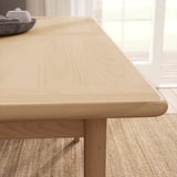 Modern light wood dining table with rounded edges and light beige textured rug.