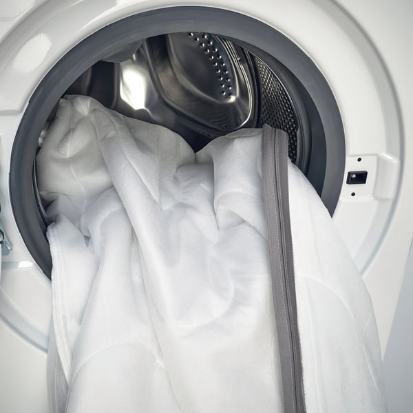Washing machine with open door, displaying a white, zipped mattress cover ready for cleaning, showcasing its machine-washable feature.