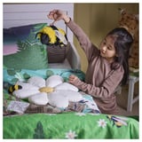 Young girl plays with soft bee toy on bed, holding it by loop, promoting imaginative play and forest awareness.