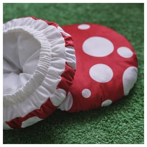 Soft mushroom-shaped cushion with white polka dots on red fabric, sitting on green carpet, showcasing quality materials and design.