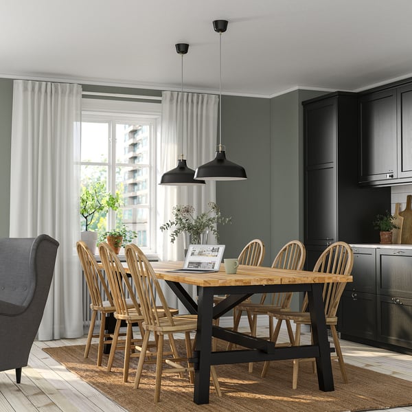 Modern kitchen SKOGSTA dining set with black-accented wooden table and spindle-back chairs near large window, surrounded by dark cabinetry.