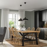 Modern kitchen SKOGSTA dining set with black-accented wooden table and spindle-back chairs near large window, surrounded by dark cabinetry.