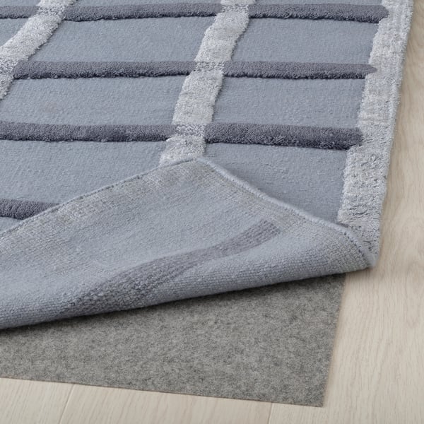 Gray handwoven rug with abstract wave pattern, shown folded on light wood floor.