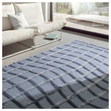 A grey, handwoven wool rug with an abstract wave pattern near a white sofa.