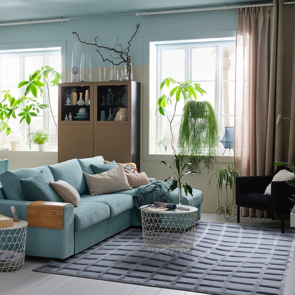 Modern living room with blue sofa, plants, & handwoven wool rug on floor, creating a cozy & stylish atmosphere.