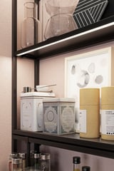 Black wall shelf with white and gold containers, clear vases, and abstract wall art.