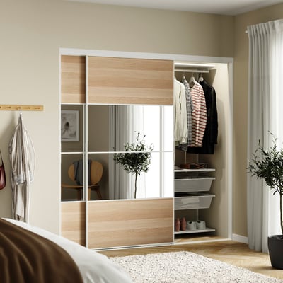 Bedroom with SKYTTA mirrored sliding closet, striped shirt, jacket, plant, thin curtains, beige walls.