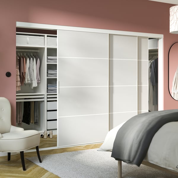 A stylish, pink-walled room with SKYTTA white closet, neatly arranged clothes, and a cozy gray rug.