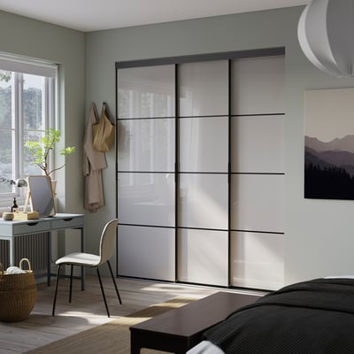 Modern bedroom with SKYTTA sliding closet doors. White with black frames, efficient space use.