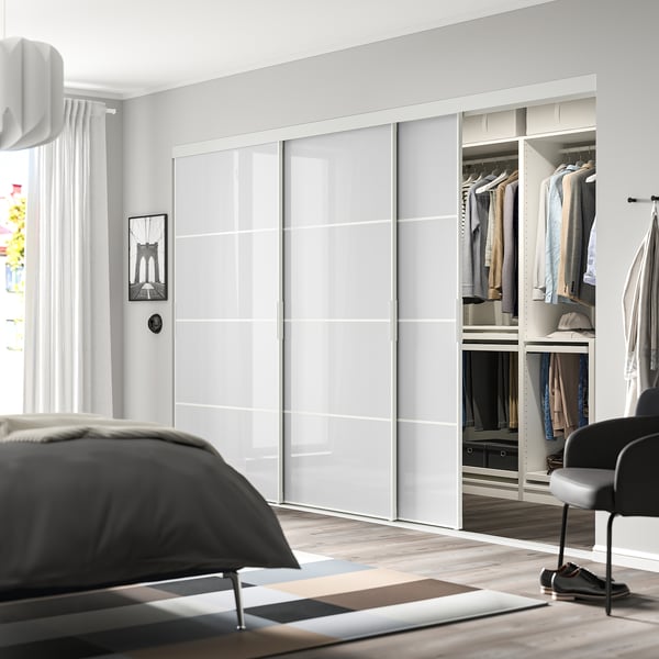 A modern bedroom with a large grey wardrobe, organized clothes, and chic chair.