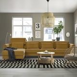 Modern living room with mustard sectional, checkered rug, coffee table, grey walls, lights, wicker chair, art.