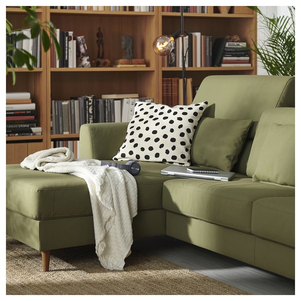 Modern olive green sofa with dot pillow, bookshelf with books, cozy setup.