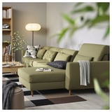 Modern olive green l-shaped sofa with adjustable cushions, a cozy blanket, and a patterned rug in a minimalist living room.