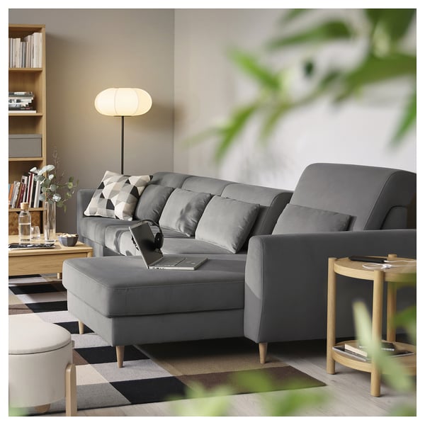 Modern grey l-shaped sofa with cushions, a laptop, and a wooden side table with a lamp.
