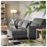 Modern grey l-shaped sofa with cushions, a laptop, and a wooden side table with a lamp.