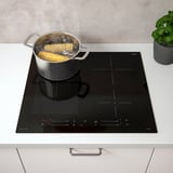 Modern kitchen with SMAKLIG induction hob cooking corn. Four zones, touch controls, and power boosters visible.