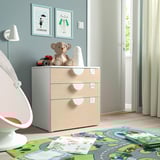 Childrens room with light blue walls, a light wooden chest of drawers, a white rocking chair, and colorful toys on the floor.